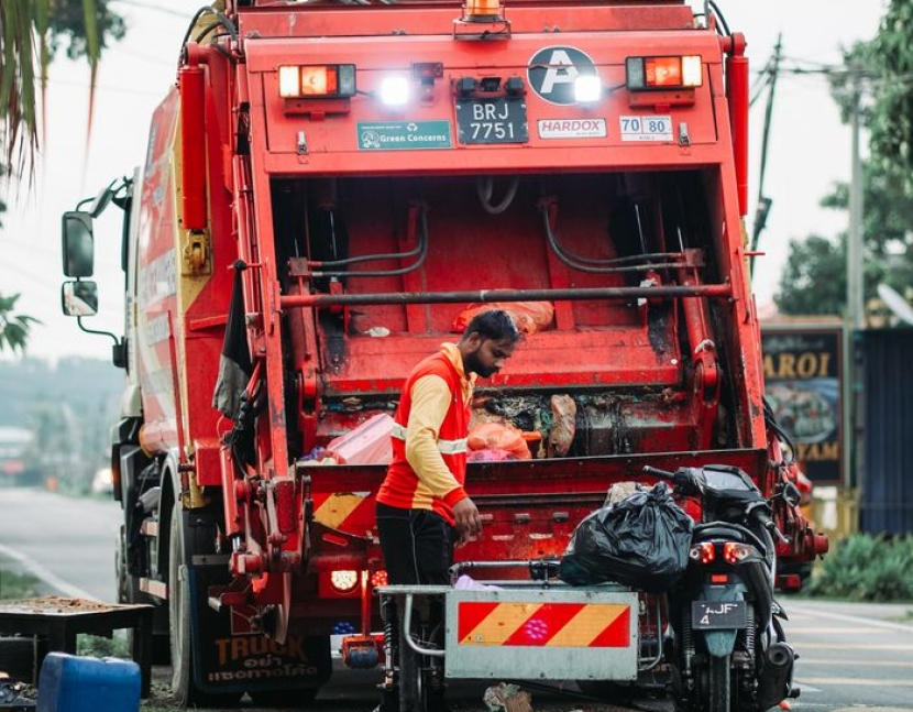 A sanitation worker managing waste disposal behind a garbage truck in Klang, Selangor.