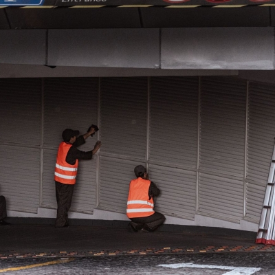Three workers in safety vests install security shutters at an indoor entrance.